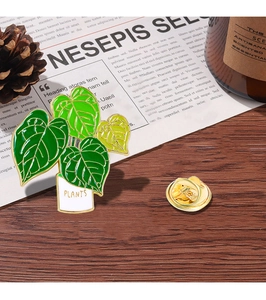 Close-up of a green plant brooch with a golden butterfly clasp on a wood background