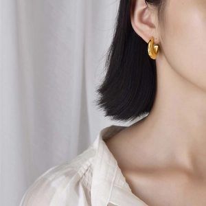 Close-up of chunky gold C-shaped hoop earring in polished stainless steel on model
