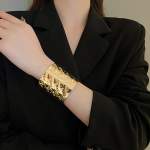 Detailed view of wide irregular hammered gold cuff bracelet worn over black sleeve