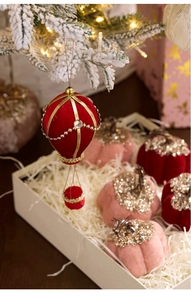 Close-up of velvet hot air balloon and pumpkin Christmas ornaments on snowy pine branches