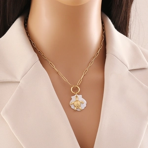 Close-up of a gold turtle necklace with white shell pendant on a model's neck