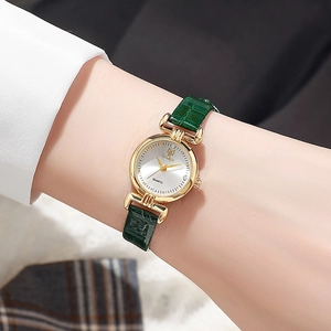 Close-up of a gold ladies quartz watch with a dark green crocodile leather strap worn on wrist