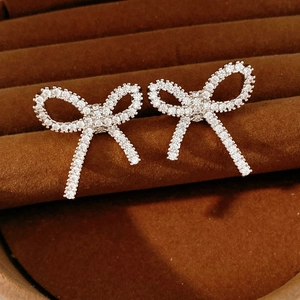 Detailed close-up of silver bow clip-on earrings with pavé zircons in a jewelry box