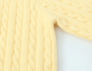 Detailed macro view of cable knit pattern on soft cream-colored knitted sweater fabric