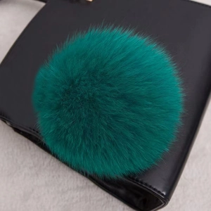 Vue détaillée d'un pompon en fourrure de renard vert foncé sur un sac à main en cuir noir