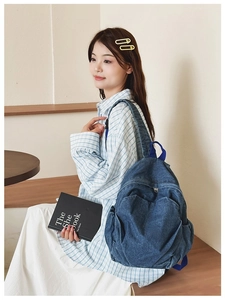 Detail of blue denim backpack showing front zipper pocket and side compartments