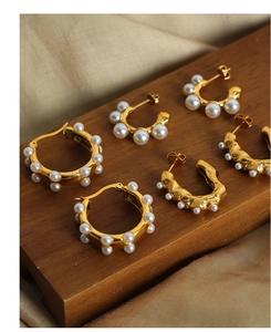 Collection of U-shaped gold pearl earrings displayed on walnut wood in vintage style