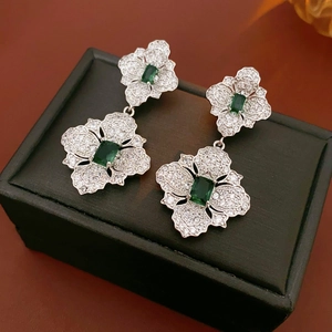 Macro view of flower-shaped silver earrings with green gems on a black jewelry box