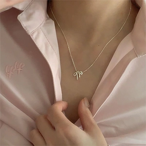 Close-up of a silver bow pendant necklace worn by a model over a pink shirt