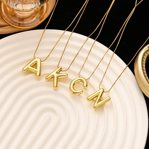 Detailed view of 3D gold initial necklaces A, K, C, N on a wavy tray with snake chains