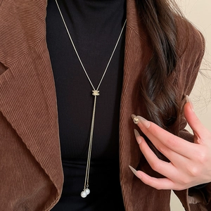 Détail du collier en Y doré avec deux perles sur un pull à col roulé noir élégant