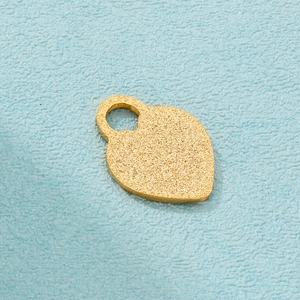 Detail of a matte gold heart-shaped handbag pendant with a round hole on a blue surface