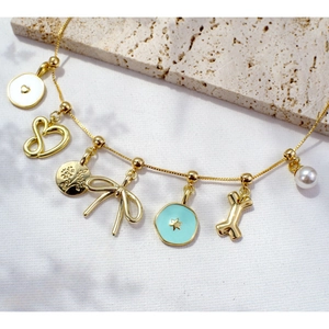 Gold-plated charm bracelet with heart, bow, star, and bone pendants on textured stone