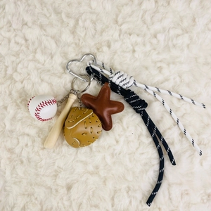 Detail of baseball keychain with mini bat, ball, glove, and braided rope on soft carpet
