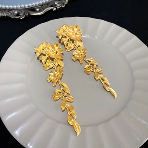 Detail of matte gold vintage floral earrings on a textured tray with a black backdrop