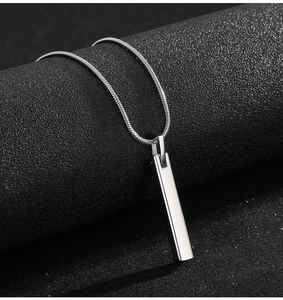 Close-up of polished silver bar pendant on a snake chain against dark textured background