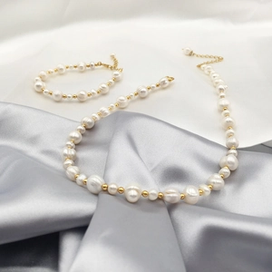 Detailed view of baroque pearl necklace and bracelet set on elegant white satin fabric