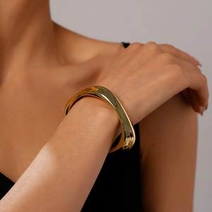 Close-up of golden irregular wavy metal bangle with polished mirror finish on wrist