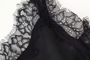Detailed close-up of delicate floral eyelash lace trim on a black satin slip dress