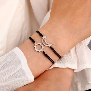 Detail of sun and moon pendants on black braided bracelets worn on wrist