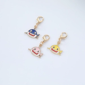 Close-up of three cute cartoon shark metal keychains in blue, pink, and yellow colors
