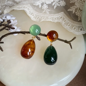 Artistic display of asymmetrical resin teardrop earrings on natural wood and jade base