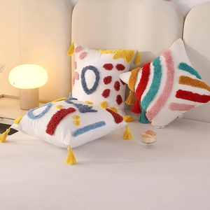 Three white tufted rainbow pillows with colorful tassels and embroidery on a cozy bed