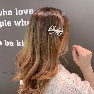 Side view of a pearl bow hair clip on brown wavy hair with elegant gold metal frame