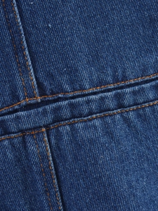 Gros plan du tissu denim bleu foncé avec doubles surpiqûres orange et texture sergée