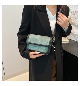Detail of grey-green suede crossbody bag with black trim and gold-tone hardware