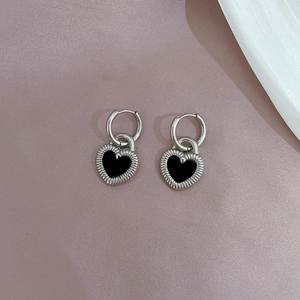 Macro shot of silver heart studs with black enamel inlay and radial metal texture