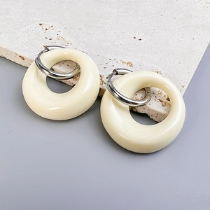 Detailed close-up of cream oval resin pendants with silver hoops on travertine stone