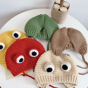 Flat lay of knit baby hats in five colors featuring 3D frog eyes and earflaps