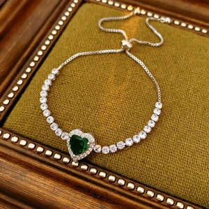 Macro shot of silver-tone bracelet with heart-shaped emerald and white zircon accents
