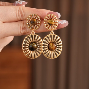 Close-up of vintage gold sunburst earrings with oval tiger eye stones being held by hand