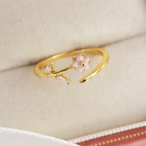 Close-up of golden adjustable ring with pink enamel flower and zircon leaves