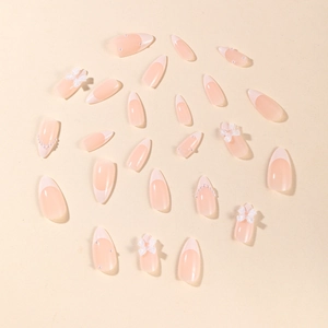 Almond shaped white French tip press-on nails with bow and pearl accents on nude pink base