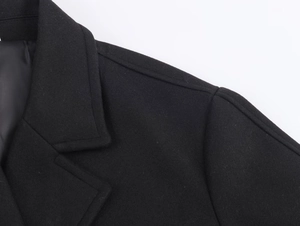 Detailed close-up of black wool coat showing shoulder stitching and fabric texture