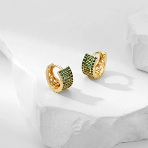 Close-up of gold huggie earrings with pavé green zircons on white stone pedestals