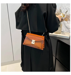 Detail of a brown crocodile texture shoulder bag with golden chain and metal clasp closure