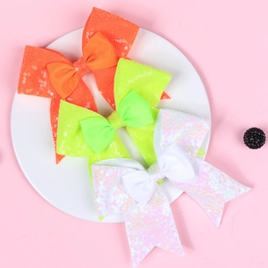 Detail of sequined bow hair clips in orange, neon green, and white on a tray