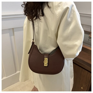 Detail of dark brown leather crescent bag with golden clasp worn on the shoulder