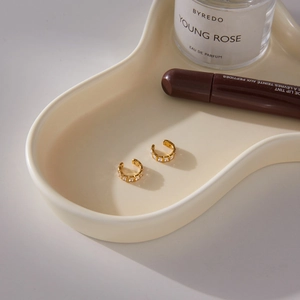 Close-up of gold plated ear cuffs with square cubic zirconia on a ceramic tray
