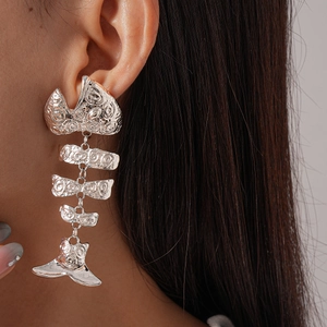 Detailed view of large silver articulated fishbone earrings on a model with metallic texture