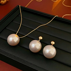 Elegant gold-plated pearl jewelry set featuring a necklace and drop earrings on black display
