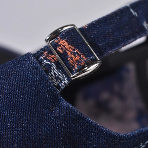 Detailed close-up of dark denim cap with silver metal buckle and orange stitching