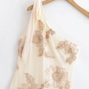 Détail d'une robe beige à broderie florale avec nœud sur l'épaule et tulle raffiné