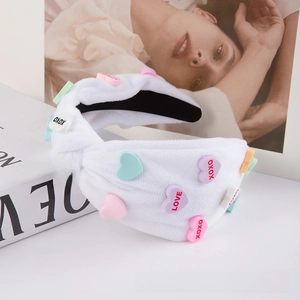 Close-up of white plush headband with colorful heart patches and XOXO LOVE text