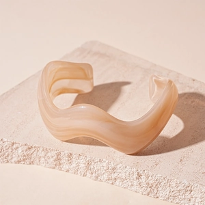 Close-up of wavy acrylic open bangle with cream marble texture on a stone pedestal