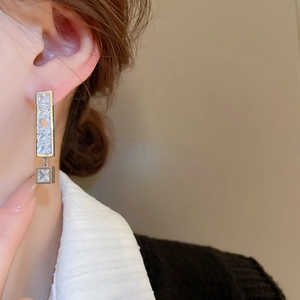 Close-up of geometric silver earrings with zircon pendants worn by a female model